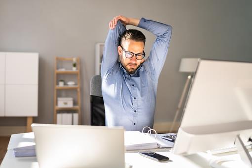 man stretching arms at desk during work